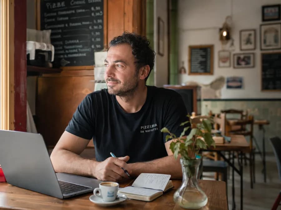 Pizzeria-Inhaber sitzt entspannt mit Laptop und Kaffee in seiner ruhigen Pizzeria